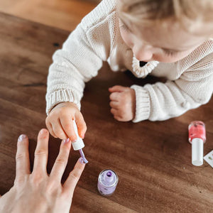 Girl painting adults finger nails with purple nail polish